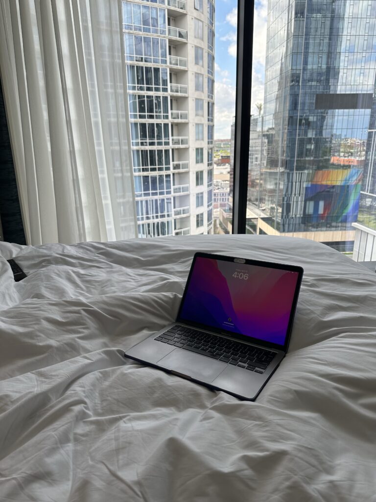 A laptop sitting on a bed, with a cityscape outside the window.